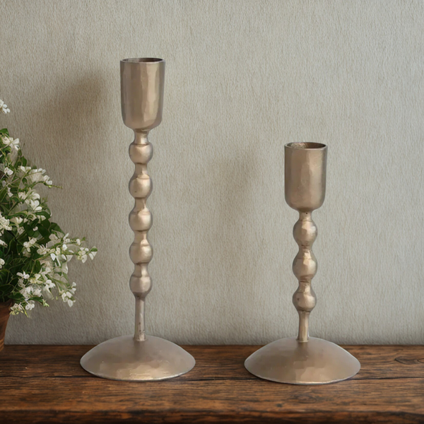 Two antique brass candle holders on a wooden surface with a neutral background
