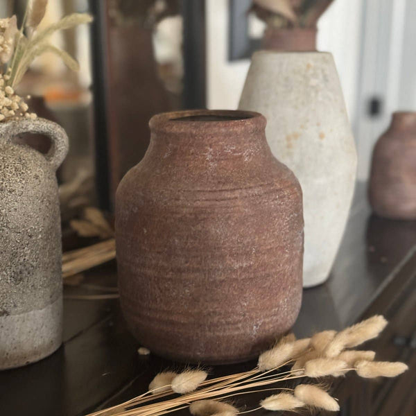 Collection of rustic ceramic vases on a reflective surface with dried plants.