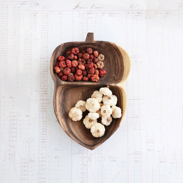 Wooden acorn-shaped bowl with red and white vase filler on a light background