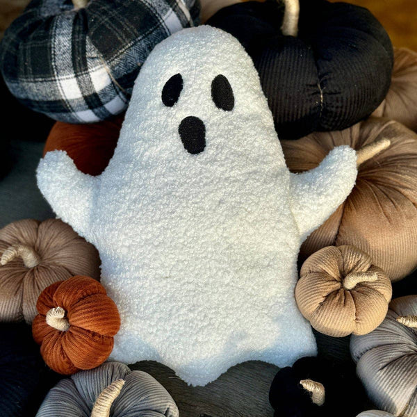 White ghost plush pillow surrounded by colorful pumpkins on a soft surface