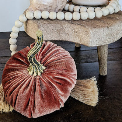 Decorative setup with a ceramic squirrel, velvet pumpkin, and lit candle on a wooden stool.