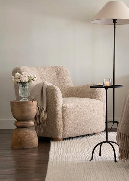 Beige armchair in a living room with a wooden side table and floor lamp.