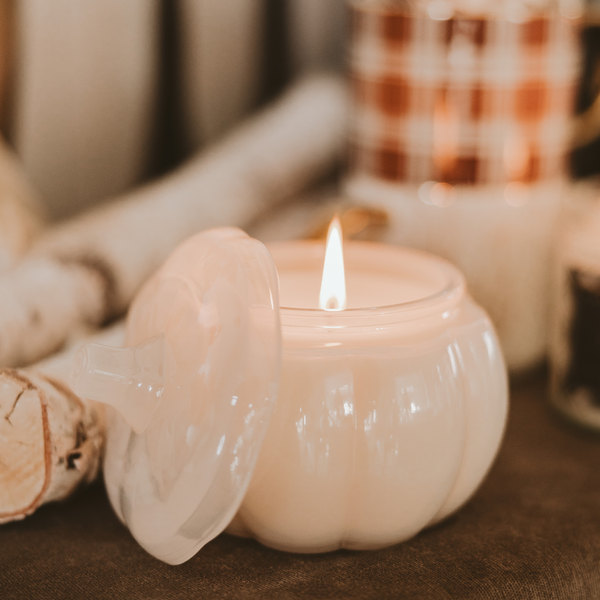 White pumpkin-shaped candle with a lit flame on a blurred background