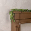 Brown fireplace mantle with faux garland against a beige wall