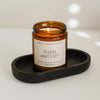 Amber glass candle with a label on a black tray against a light background