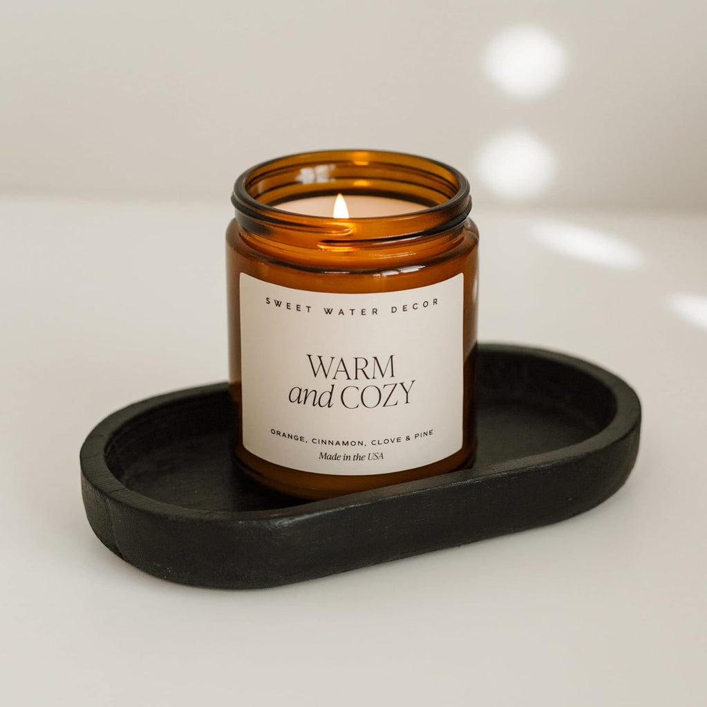 Amber glass candle with a label on a black tray against a light background