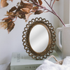 Decorative mirror with scalloped design on a surface with books and a mug.