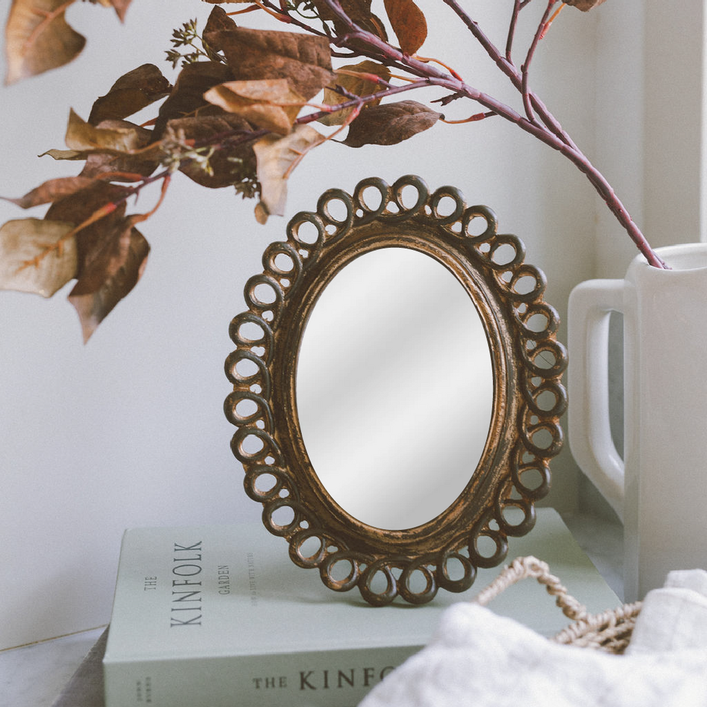 Decorative mirror with scalloped design on a surface with books and a mug.