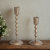 Two antique brass candle holders on a wooden surface with a neutral background