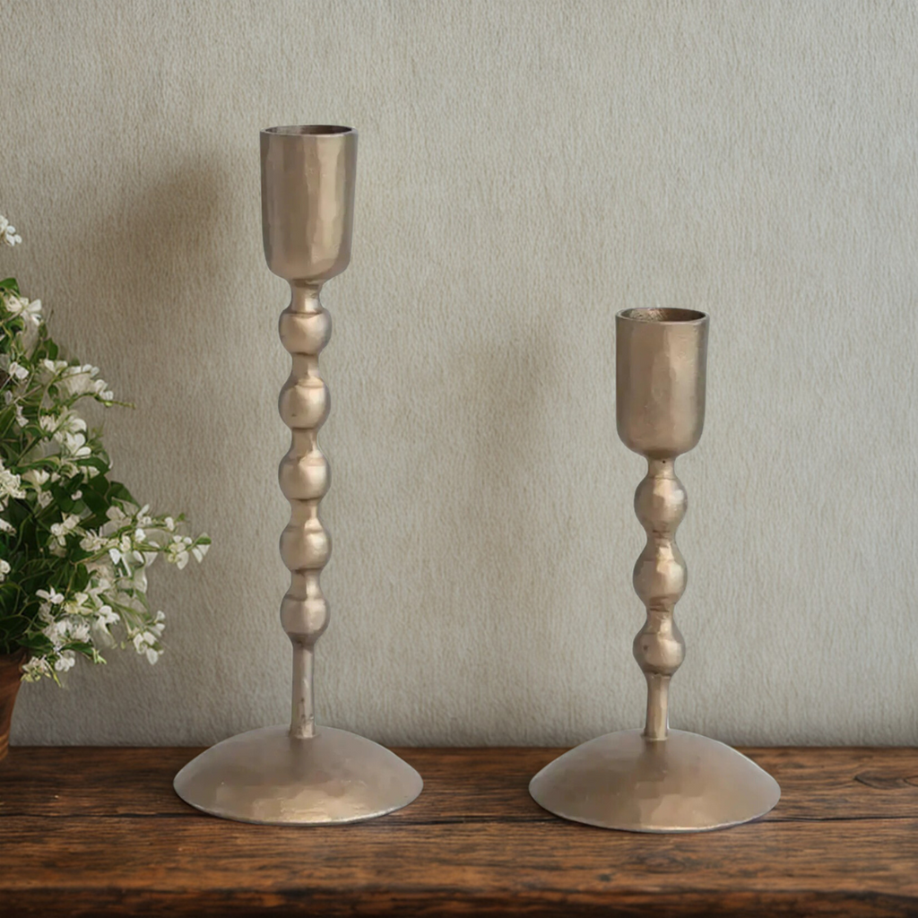 Two antique brass candle holders on a wooden surface with a neutral background