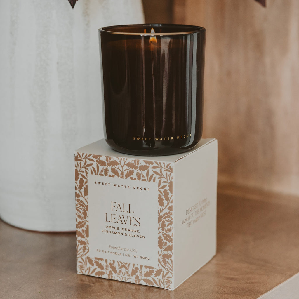 Amber Glass fall candle on a decorative box labeled 'Fall Leaves' with a blurred background