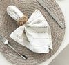 Table setting with woven placemat, striped napkin, and cutlery on a neutral background