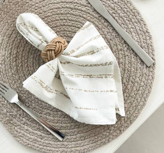 Table setting with woven placemat, striped napkin, and cutlery on a neutral background