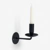 Black wall-mounted candle holder with a white candle on a white background