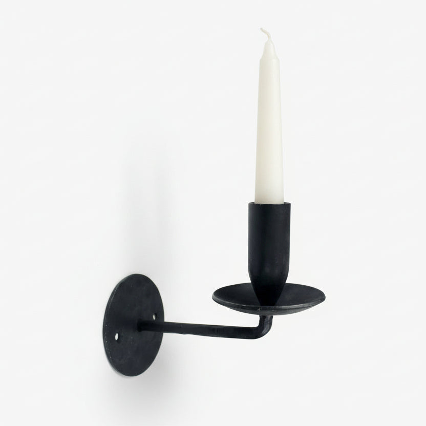 Black wall-mounted candle holder with a white candle on a white background
