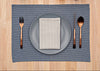 Dining table setting with gray plate, striped napkin, cutlery, and blue placemat on a wooden surface.
