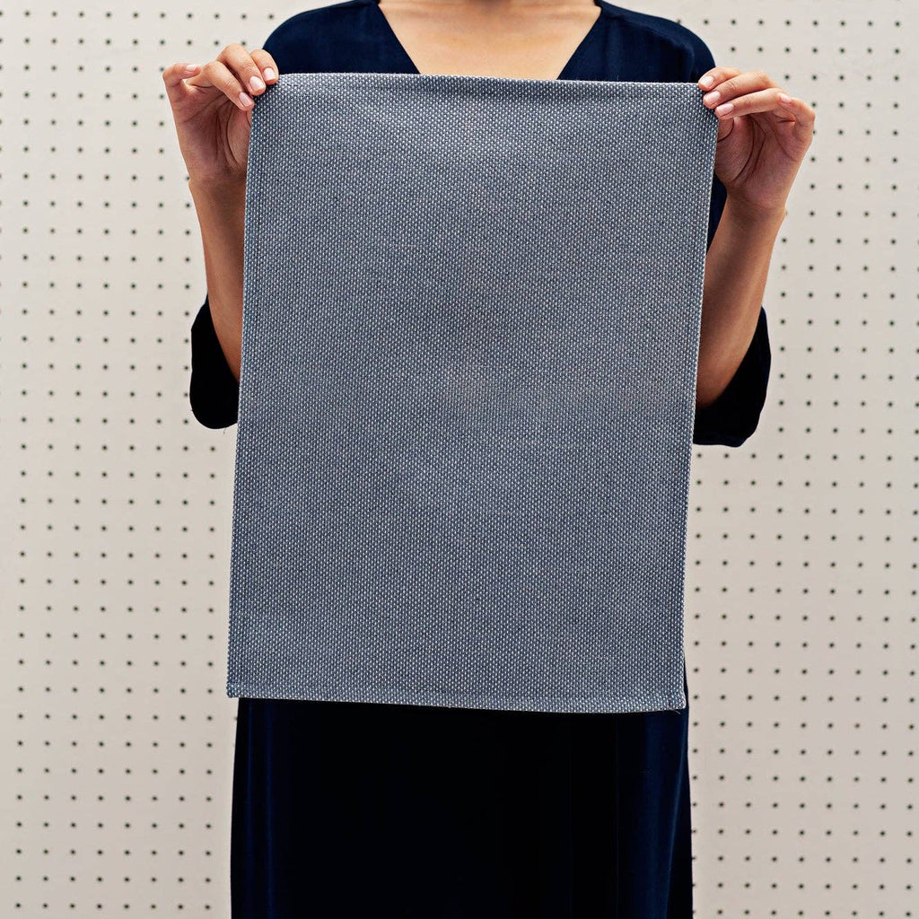 Woman holding a blue textured placemat against a light background
