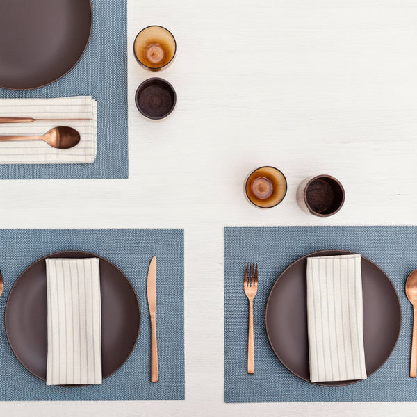 Table settings with blue cotton placemats, plates, cutlery, and decorative elements.