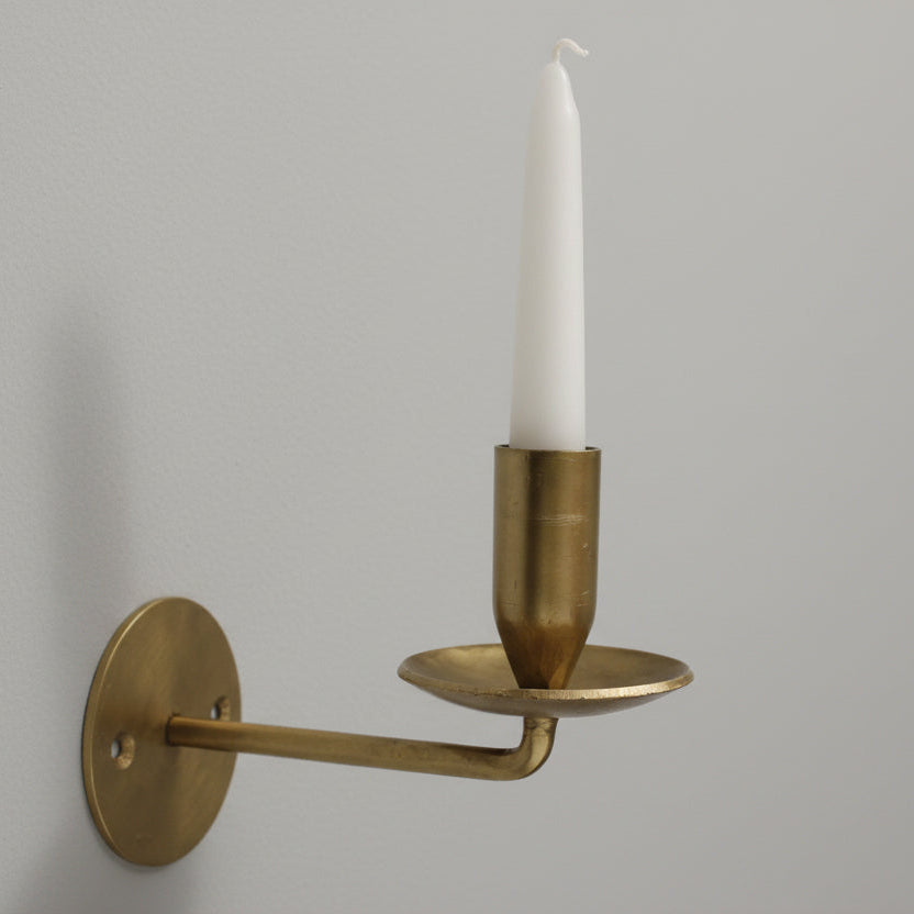 Brass wall-mounted candle holder with a white candle on a gray background