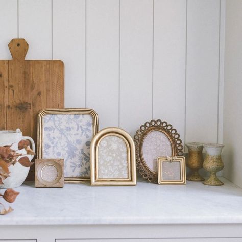 Decorative photo frames and vases on a white surface with a wooden wall background