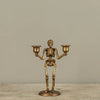 A brass skeleton candlestick holder with two cup-shaped candle holders, standing on a round base against a plain beige background.