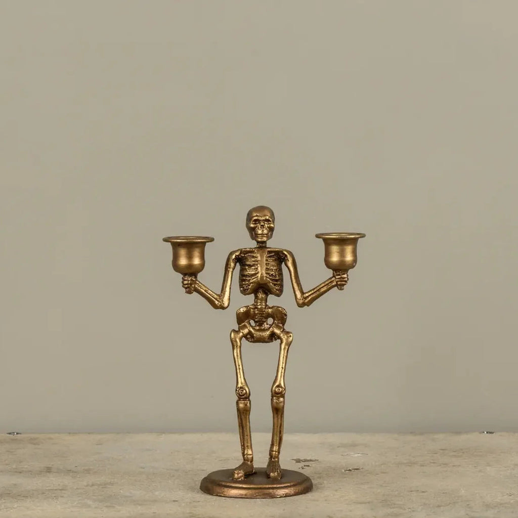 A brass skeleton candlestick holder with two cup-shaped candle holders, standing on a round base against a plain beige background.
