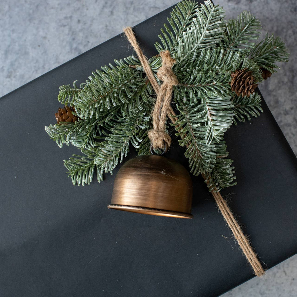 Bronze bell with green pine branch and twine on a dark surface