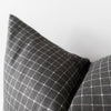 Close-up of a dark gray throw pillows with a white windowpane plaid pattern, set against a plain light gray background.
