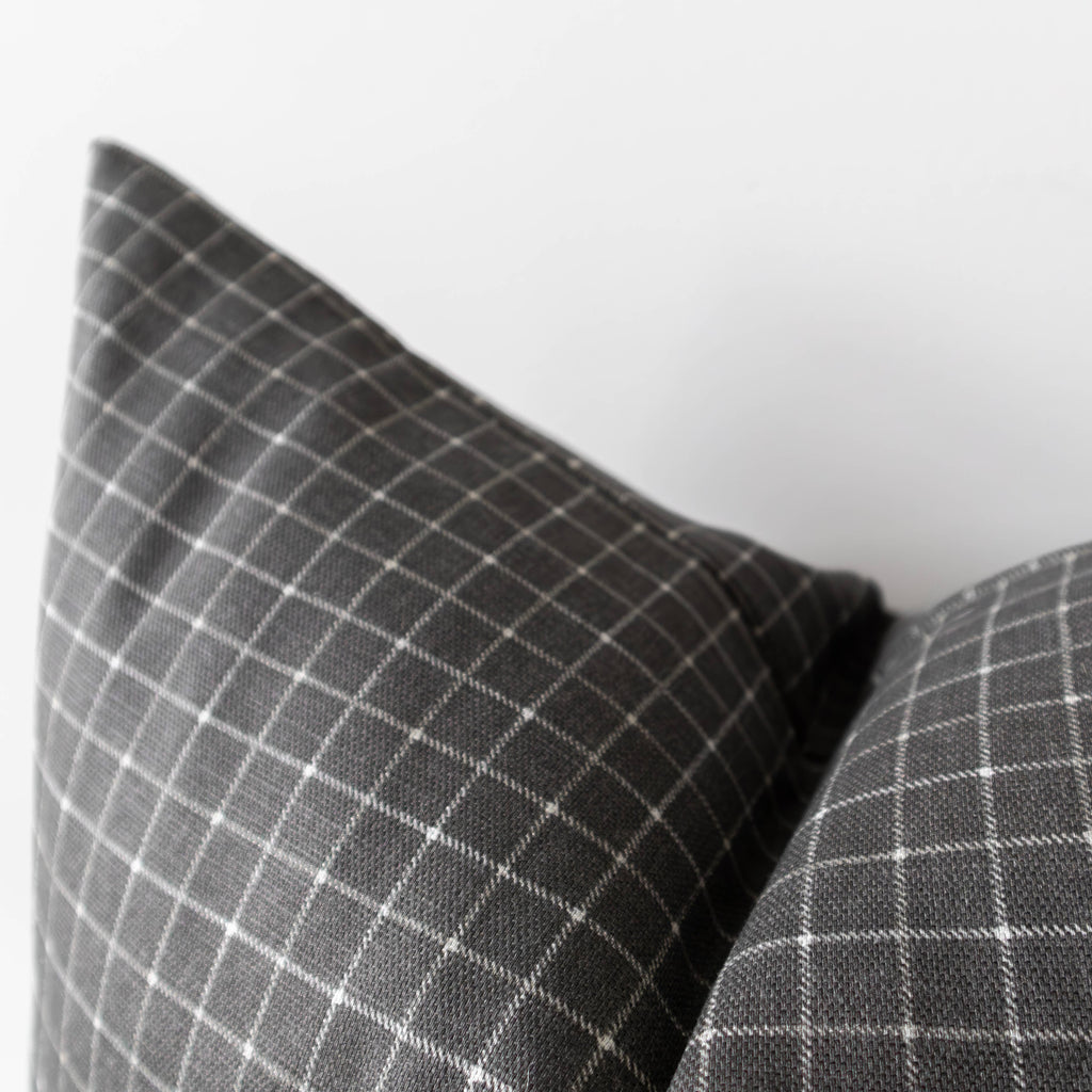 Close-up of a dark gray throw pillows with a white windowpane plaid pattern, set against a plain light gray background.