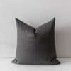 A square throw pillow in dark gray fabric with a fine white windowpane grid pattern, standing upright against a light gray background.