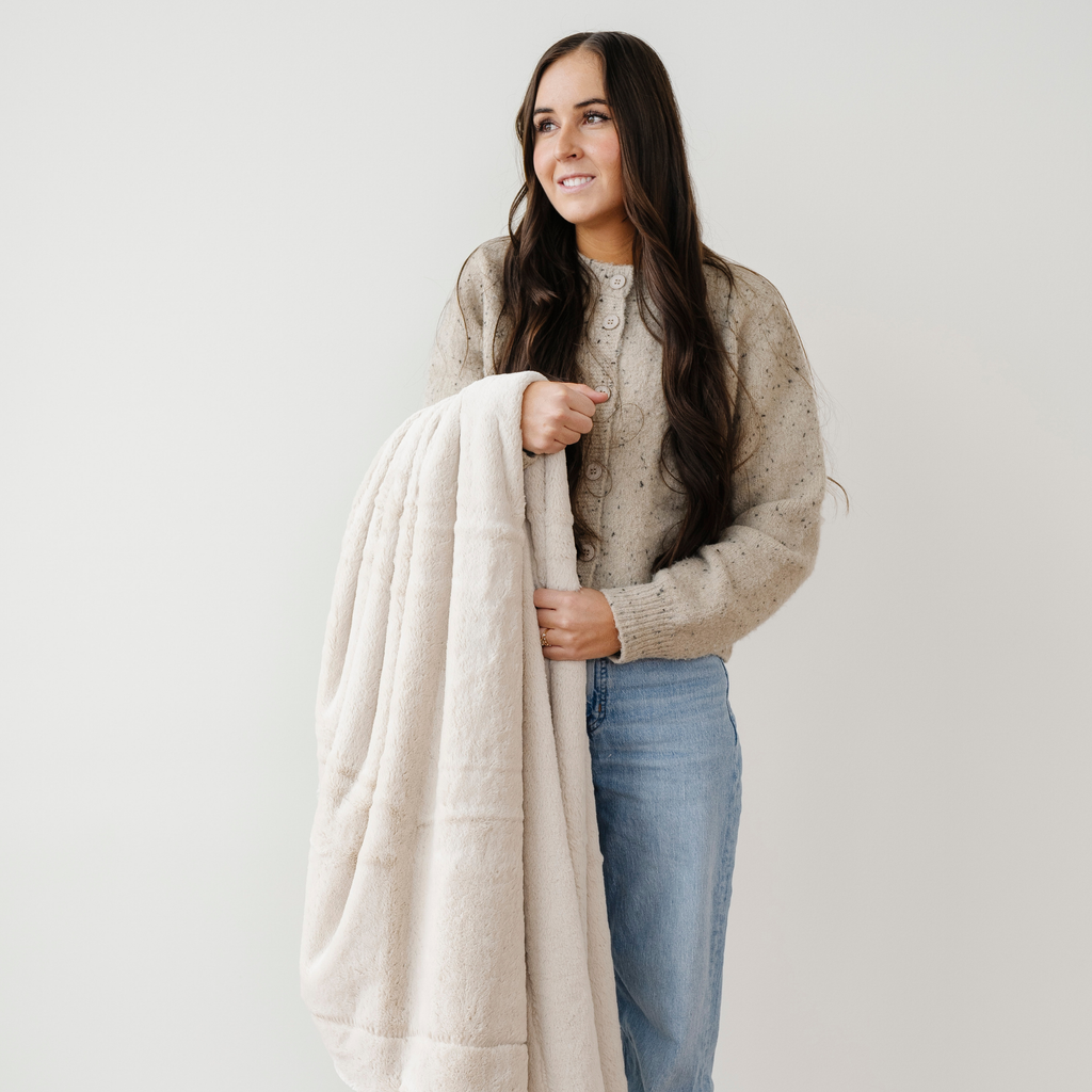 Woman holding a beige blanket against a plain background
