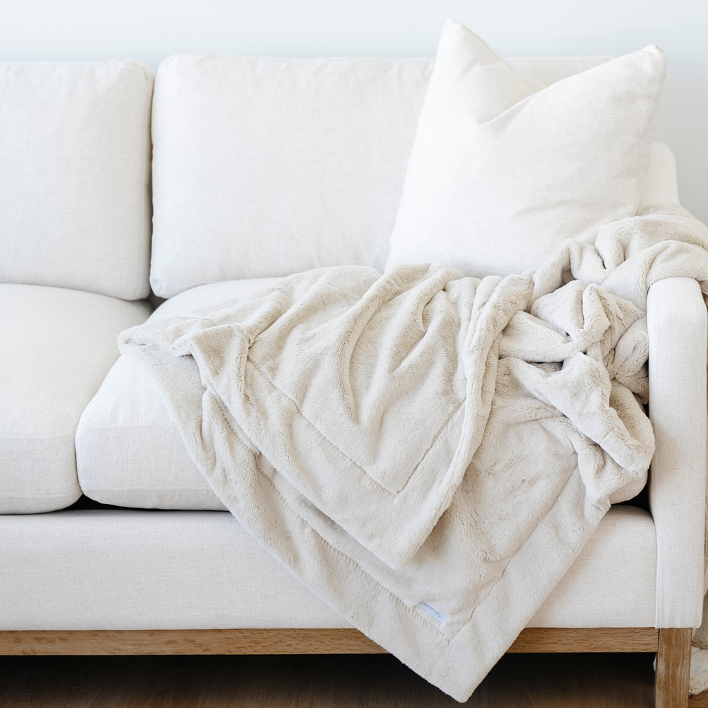 Beige blanket draped over a white sofa with a white pillow.