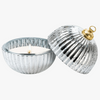 A silver ribbed glass candle jar with a matching lid, shown on a white background. The lid is propped up next to the open jar, which contains a white candle and a small flame.