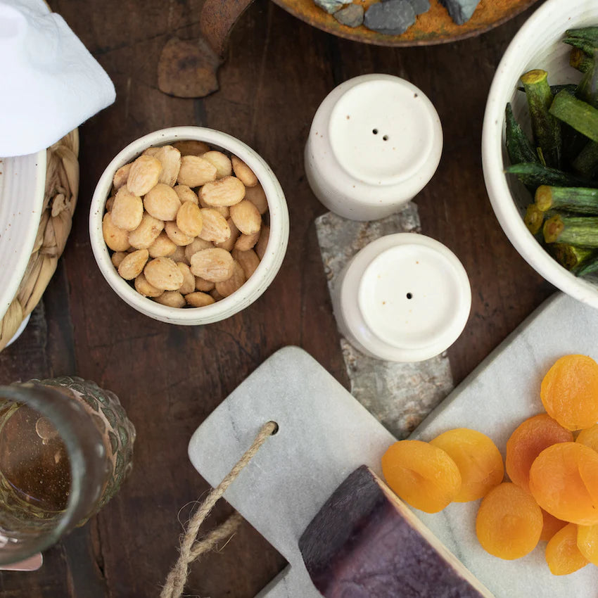 Assorted snacks including dried apricots, nuts, and green beans on a wooden table with salt and pepper shakers.