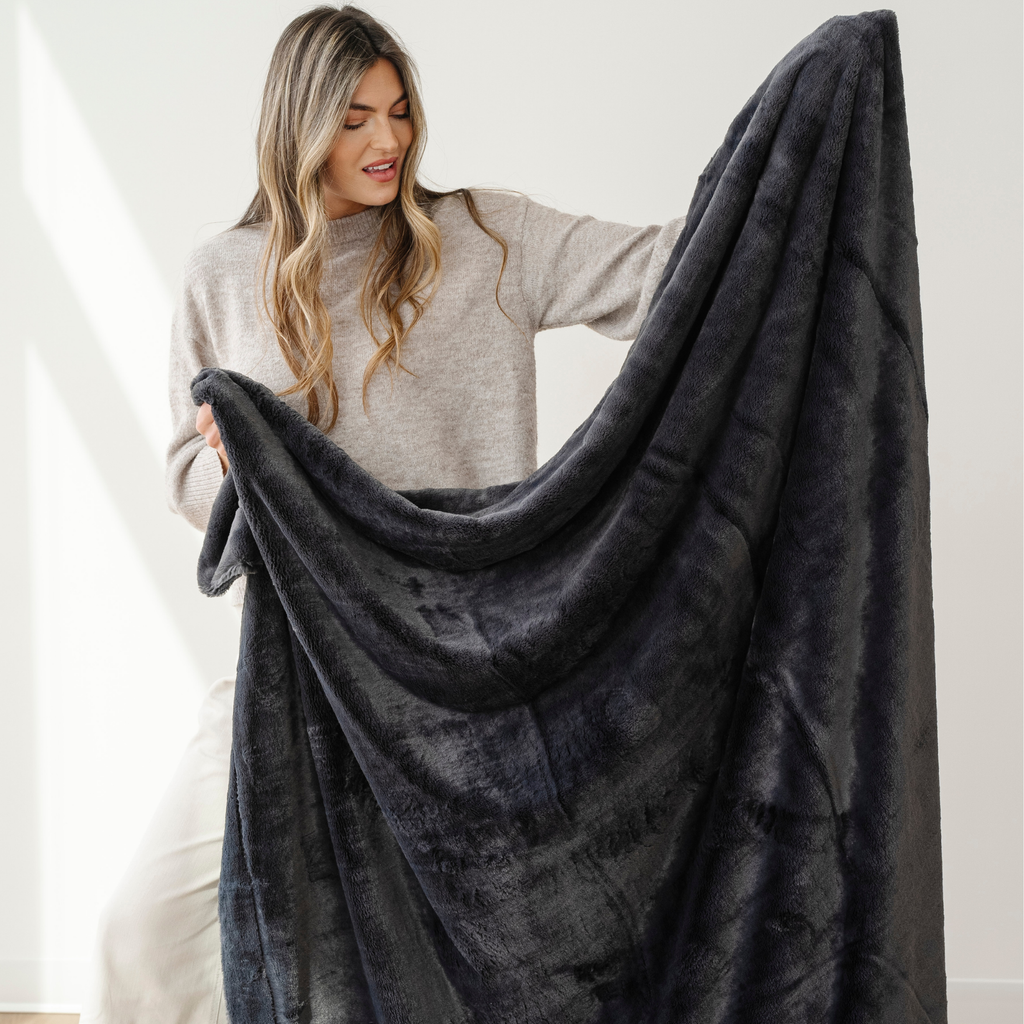 Woman holding a large dark gray blanket against a white background