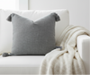 Gray pillow with tassels on a white sofa in a living room setting.