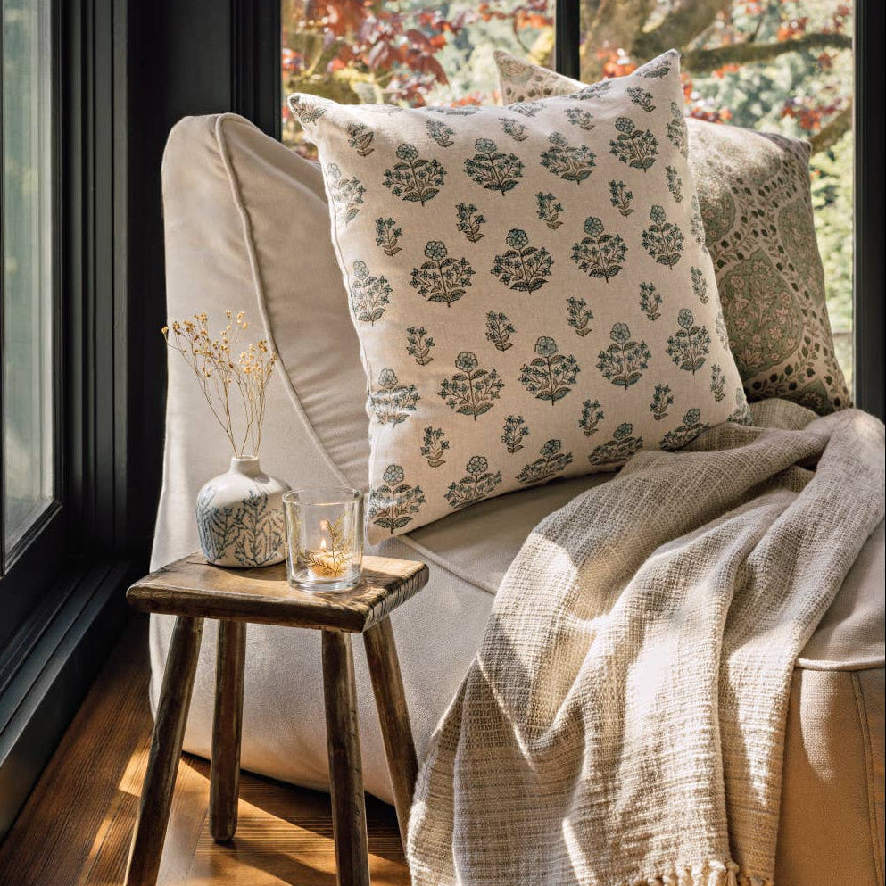 Cozy corner with a sofa, decorative pillows, and a small table by a window with autumn foliage.