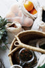 Mesh product bags with oranges and other items on a wooden surface, with a woven basket and teacup in the foreground.