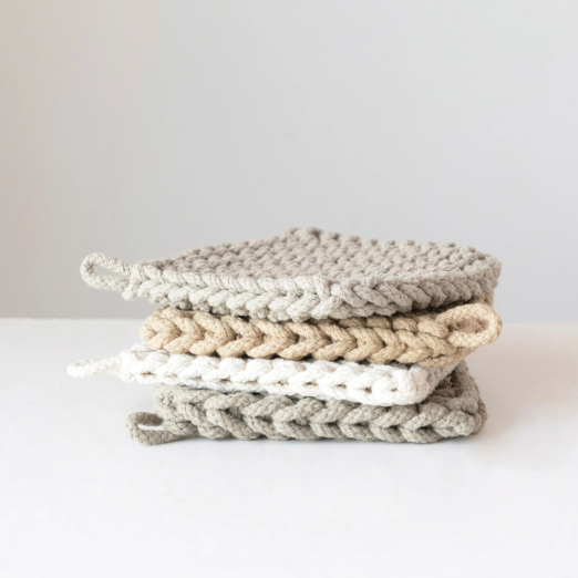 Stack of square, chunky-knit neutral colored pot holders in a kitchen setting with white background.