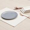Gray plate on a cream cotton placemat with silverware and napkins on a light wooden surface