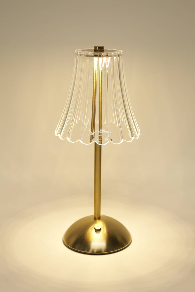 Table lamp with a clear glass shade and gold base on a neutral background