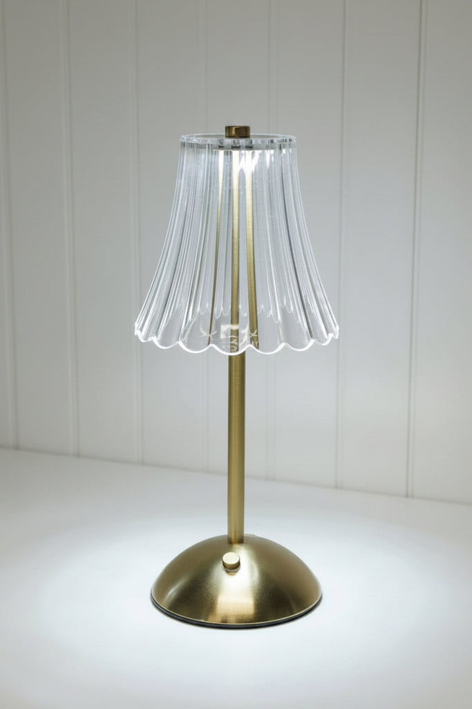 Small table lamp with pleated glass shade on a surface with books and shiplap in the background