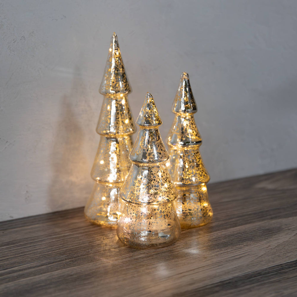 Decorative glass Christmas trees with lights on a wooden surface.
