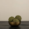 Decorative arrangement with moss balls in a brass bowl, sunflowers, and a white vase on a wooden surface.