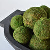 Green moss balls arranged in a dark gray ceramic bowl on a white background.