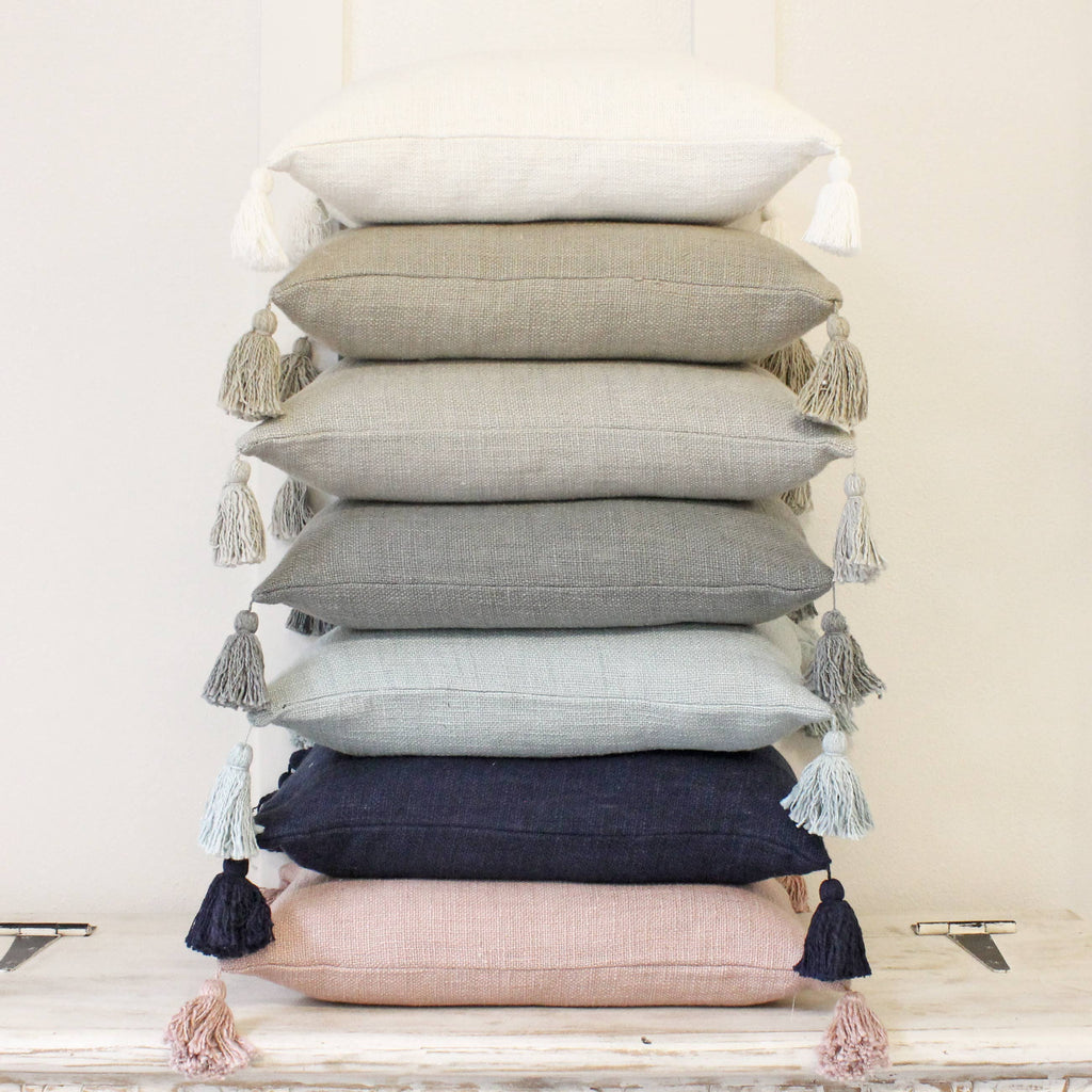 Stack of decorative throw pillows with tassels on a wooden surface