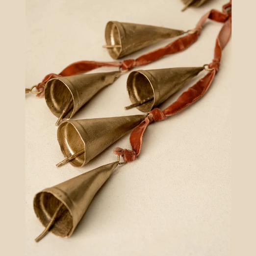 Decorative string of brass bells with red velvet ribbon on a beige background