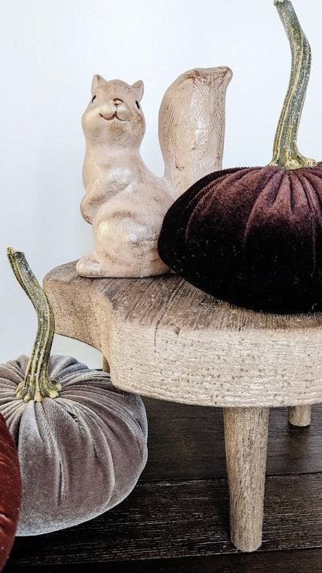 Decorative squirrel figurine and velvet pumpkins on a wooden surface with a white background
