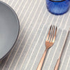 Table setting with a gray plate, blue mug, and cutlery on a striped placemat.