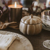 Decorative pumpkin-shaped candle on a wooden surface with candles in the background